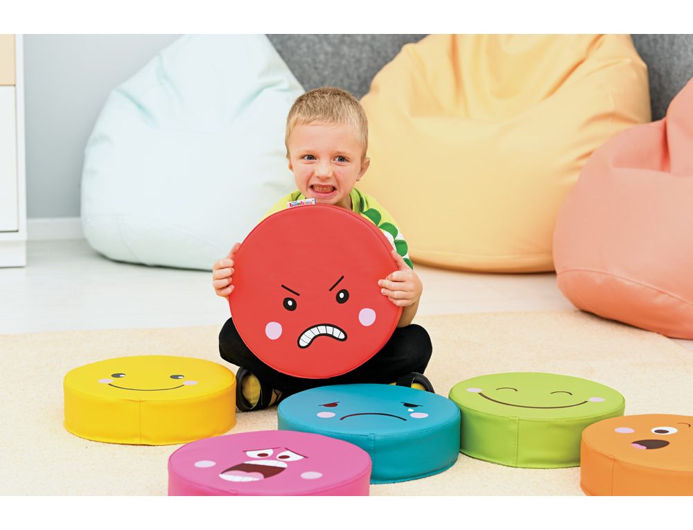 Chlapec sedí na podlaze a drží červený polštář s naštvaným obličejem. Kolem něj jsou barevné polštářky s různými emocemi. Edukační hračka pro děti na rozpoznávání a vyjadřování emocí, vhodná do mateřských škol a herních koutků.