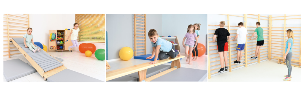 Děti si hrají a sportují v tělocvičně s různými pomůckami, jako jsou trampolíny, balanční desky a žebřiny.