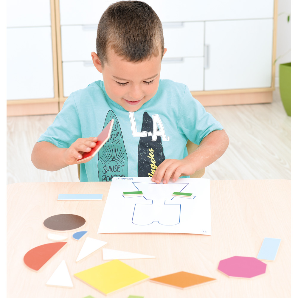 Chlapec přiřazuje barevné geometrické tvary k předloze na papíře.