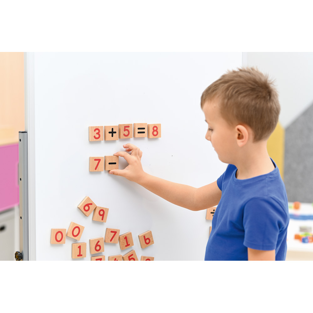 Chlapec skládá dřevěné magnetické kostky s čísly a matematickými znaky.