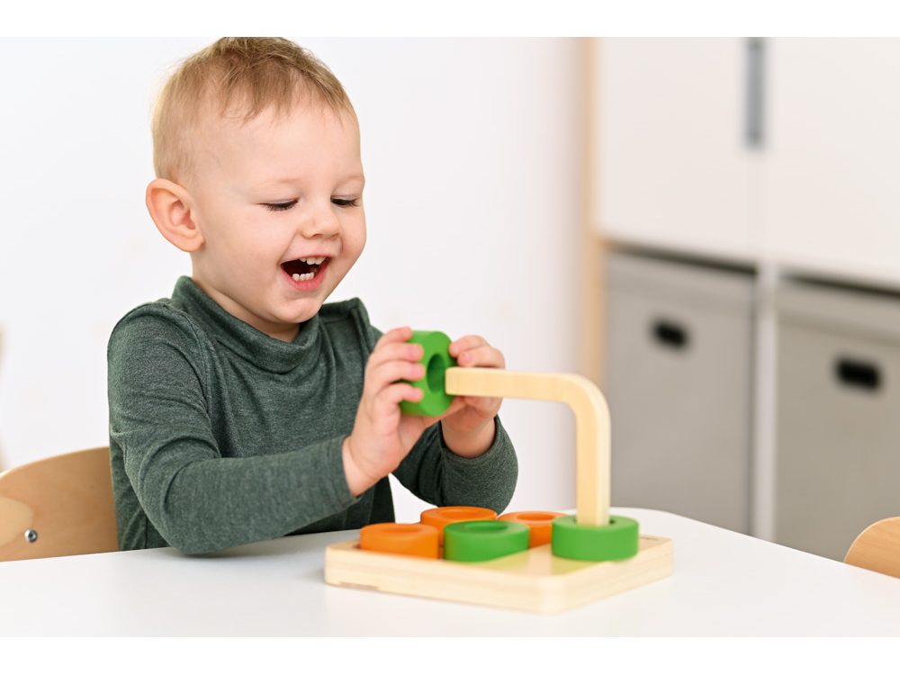Batole manipuluje s barevnými dřevěnými tvary na montessori pomůcce, učí se logickému myšlení a vztahu mezi tvary a prostorem.
