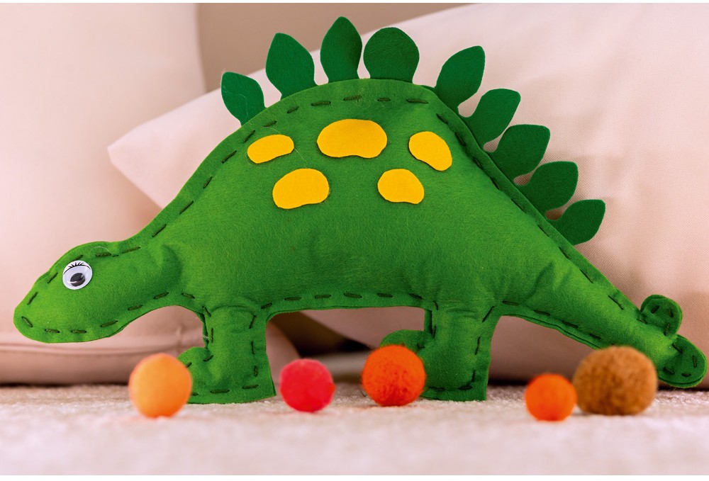 Ručně vyrobený plyšový dinosaurus s jasně zelenou barvou, sedící mezi barevnými koulemi na měkkém podkladu.