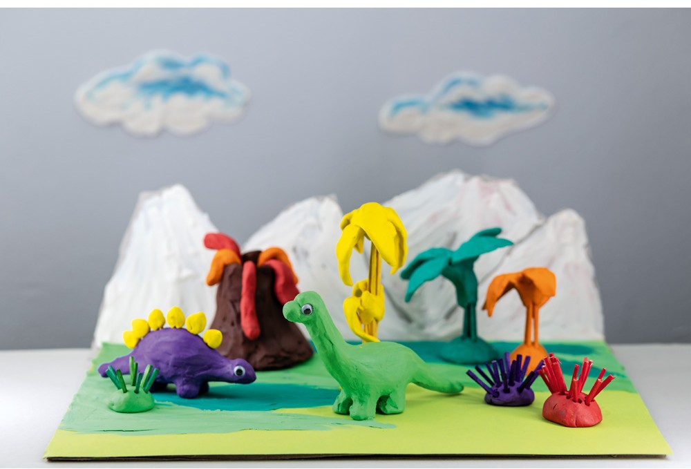 Kreativní modely dinosaurů vyrobené z plastelíny, vystavené na stole mezi různými přírodními prvky.
