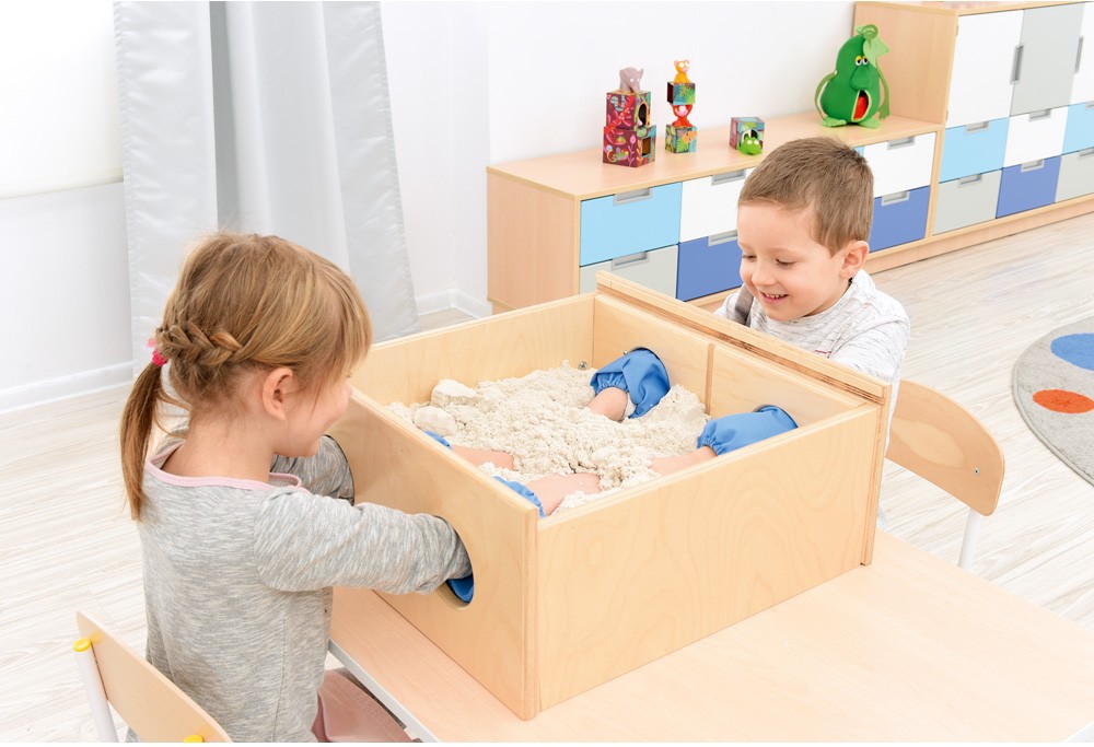 Dvě děti si hrají s pískem v dřevěném senzorickém boxu a společně objevují různé textury