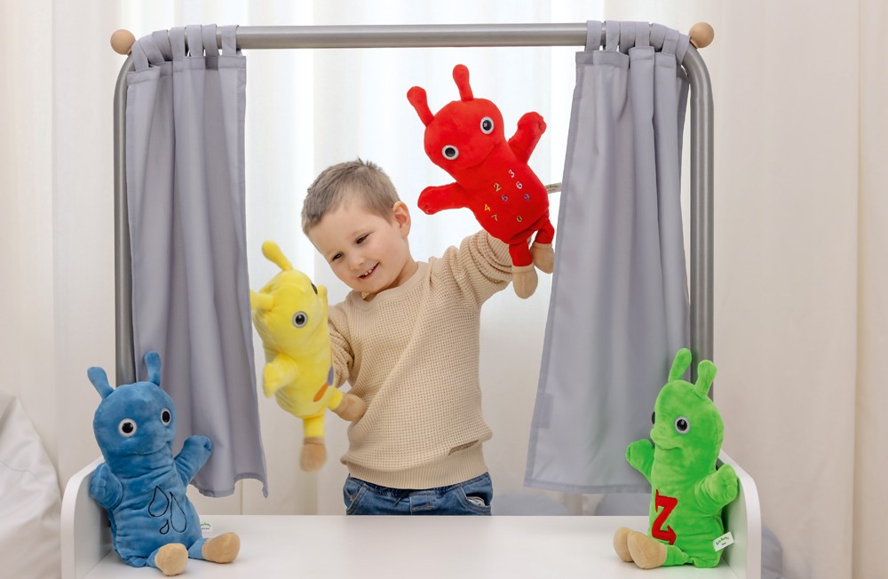 Chlapec si hraje s barevnými maňásky za malým divadlem s oponou