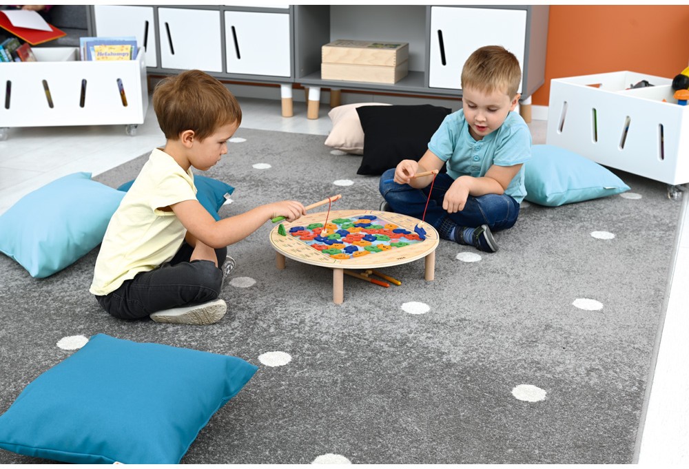 Dvě děti loví barevné rybičky pomocí udic na herní podložce v mateřské škole.