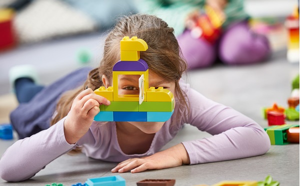 dziewczynka patrzy przez okno zbudowanego przez siebie modelu z klocków lego duplo